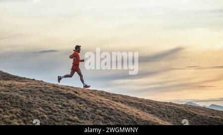 L'uomo sportivo corre in discesa tra le montagne sul prato Foto Stock