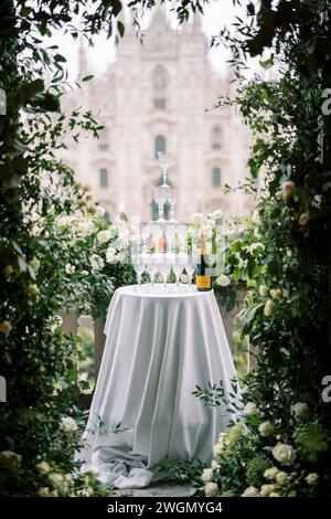 Pila di bicchieri su un tavolo accanto a una bottiglia di champagne su un balcone coperto di rose che si affaccia sul Duomo. Milano, Italia Foto Stock