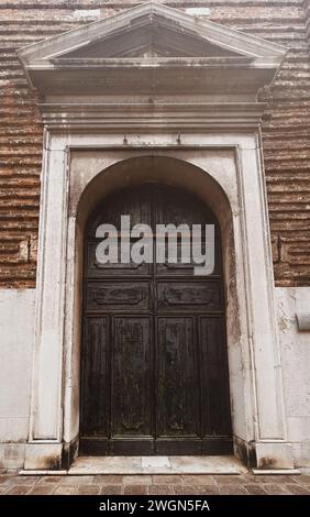 I sussurri della storia veneziana riecheggiano attraverso i grani intemprati di questa vecchia porta in legno, una silenziosa testimonianza di secoli di storie all'interno del labirinto di Venezia Foto Stock