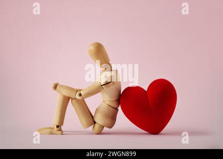 Manichino in legno seduto con cuore su sfondo rosa - concetto d'amore Foto Stock