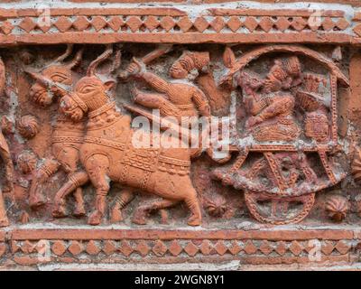 Vista ravvicinata della scena in terracotta intagliata con uomini che cavalcano un carro di cavalli sull'antico tempio Govinda nel complesso religioso Puthia, Rajshahi, Bangladesh Foto Stock