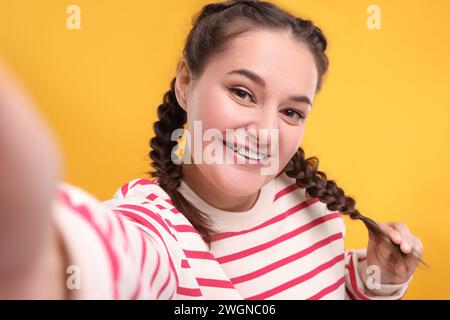 Donna sorridente con l'apparecchio che scatta selfie su sfondo arancione Foto Stock