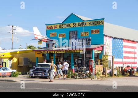 I turisti esplorano un nostalgico negozio sulla Route 66 a Seligman, Arizona, che è adornato da cartelli colorati e un murale con bandiera americana. Foto Stock