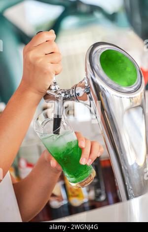 Un barista versa birra verde in una tazza di vetro in un bar durante un St. Festa di Patrick Foto Stock