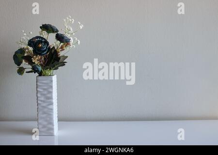 Decorazione domestica sotto forma di vaso con fiori artificiali. Bouquet di rose blu e un ramo di fiori bianchi sembrano esteticamente piacevoli Foto Stock