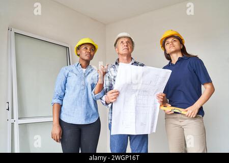 Gruppo eterogeneo di operaie edili e architetto con progetto interno all'interno dell'hotel Foto Stock