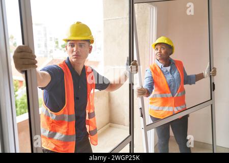 Falegnami multietnici per l'installazione di telai per finestre Foto Stock