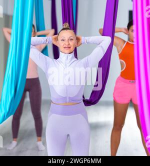 Donna sportiva che fa ginnastica articolare prima dell'allenamento di gruppo di yoga aereo Foto Stock