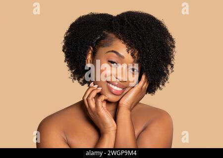 Contenuto donna nera con mani sul viso, capelli ricci, sfondo beige Foto Stock