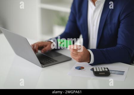 Uomo d'affari maturo in un elegante blazer blu che effettua un pagamento online con una carta di credito verde Foto Stock