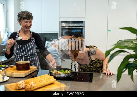 Un gruppo misto di amiche che preparano cibo da festa in una cucina moderna Foto Stock