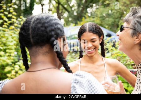 Una donna bianca matura chatta e ride con due giovani donne nere a una festa in giardino Foto Stock