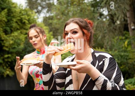 Due giovani Trans donne che si divertono e mangiano cibo da festa e si godono una festa estiva in giardino Foto Stock