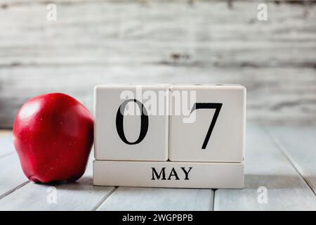 Blocchi di calendario in legno bianco con la data del 7 maggio e una mela rossa per il National Teacher Appreciation Day. Foto Stock