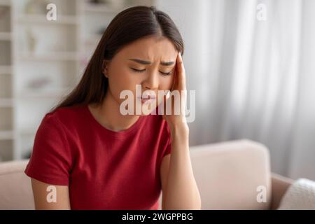 Donna asiatica con forte mal di testa che si sente male a casa Foto Stock