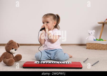 Una bambina carina che canta con il pianoforte giocattolo e il microfono a casa Foto Stock