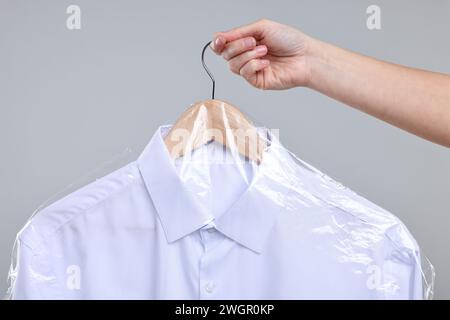 Servizio di lavaggio a secco. Donna che tiene la camicia in una busta di plastica su sfondo grigio, primo piano Foto Stock