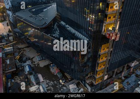 Un grattacielo in costruzione di sera, decorato con pareti di vetro, con un gran numero di strutture ingegneristiche in funzione Foto Stock