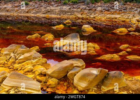 I caldi depositi minerali arancioni del Rio Tinto scolpiscono un paesaggio strutturato con pozzanghere riflettenti Foto Stock