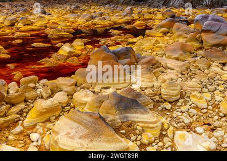 I caldi depositi minerali arancioni del Rio Tinto scolpiscono un paesaggio strutturato con pozzanghere riflettenti Foto Stock