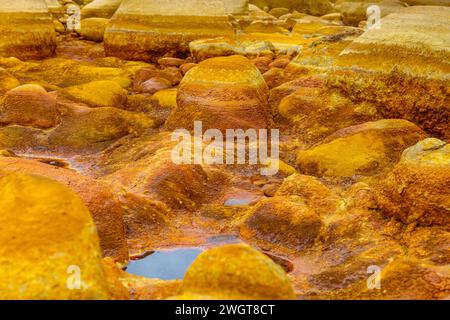 I caldi depositi minerali arancioni del Rio Tinto scolpiscono un paesaggio strutturato con pozzanghere riflettenti Foto Stock