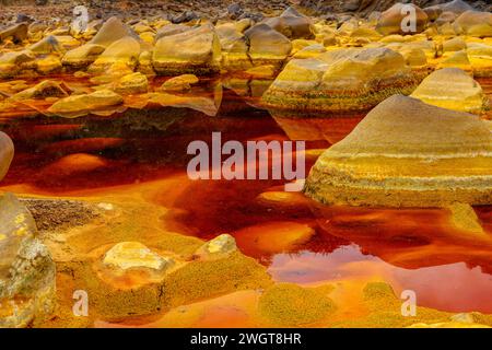 Pietre rivestite di ferro a strati emergono dalle acque acide e rossastre nell'esclusivo paesaggio del Rio Tinto Foto Stock