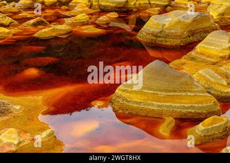 Pietre rivestite di ferro a strati emergono dalle acque acide e rossastre nell'esclusivo paesaggio del Rio Tinto Foto Stock