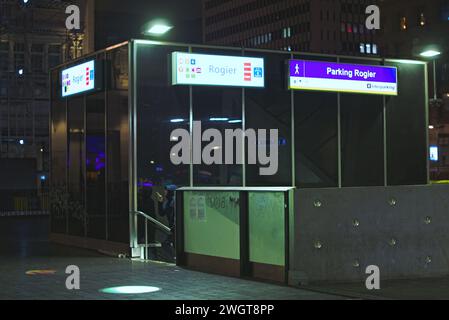 Bruxelles, Belgio. 5 febbraio 2024. Ingresso alla metropolitana. Passeggero al telefono in metropolitana di notte. Stazione Roger. Grattacielo sullo sfondo Foto Stock