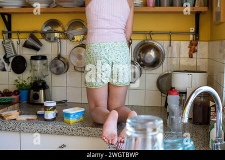 Giovane ragazza in equilibrio sul lato della cucina mettendo via i piatti Foto Stock