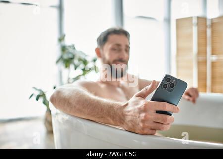 concentrati su uno smartphone moderno nelle mani di un uomo barbuto sfocato che fa il bagno, salute mentale Foto Stock