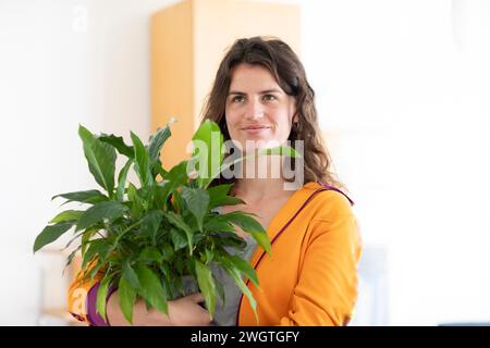 giovane donna con giacca gialla e pianta verde a casa Foto Stock