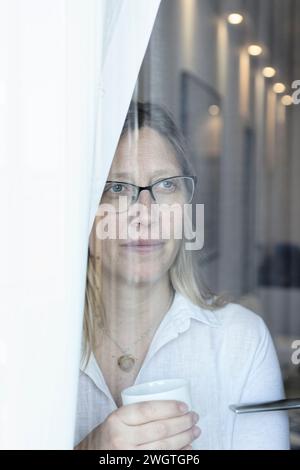 Donna bionda che guarda fuori dalla finestra, Milano, Italia. Foto Stock