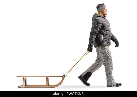 Foto a tutta lunghezza di un uomo con una giacca invernale che cammina e tira una slitta di legno isolata su sfondo bianco Foto Stock