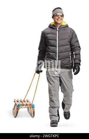 Ritratto di un uomo in una giacca invernale che cammina e tira una slitta di legno isolata su sfondo bianco Foto Stock
