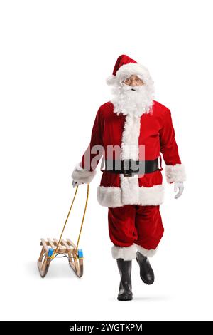 Babbo Natale cammina verso la telecamera e tira una slitta di legno isolata su sfondo bianco Foto Stock
