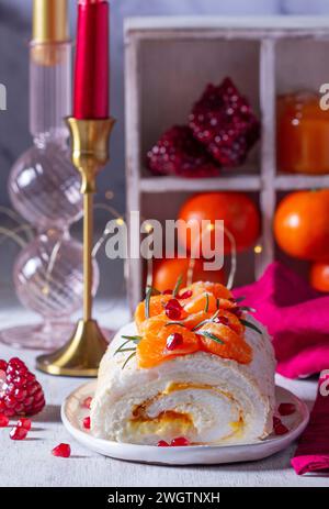 Rotolo di meringa ripieno di mascarpone, crema e marmellata di mandarini, decorato con mandarini e semi di melograno. Dessert per San Valentino, mandarino Foto Stock