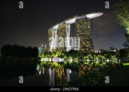 L'iconico Marina Bay Sands Resort and Hotel con una piscina in primo piano vicino ai Gardens by the Bay illuminata brillantemente, Singapore Foto Stock