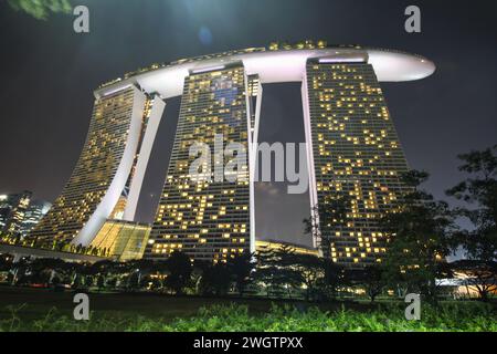 Le triple torri dell'hotel Marina Bay Sands sono completamente illuminate e si innalzano maestosamente contro il cielo notturno evidenziando lo skyline di Singapore Foto Stock