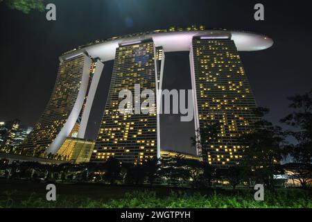 Le triple torri dell'hotel Marina Bay Sands sono completamente illuminate e si innalzano maestosamente contro il cielo notturno evidenziando lo skyline di Singapore Foto Stock