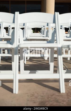 File di sedie pieghevoli bianche disposte all'aperto accanto alle colonne all'esterno di un edificio Foto Stock