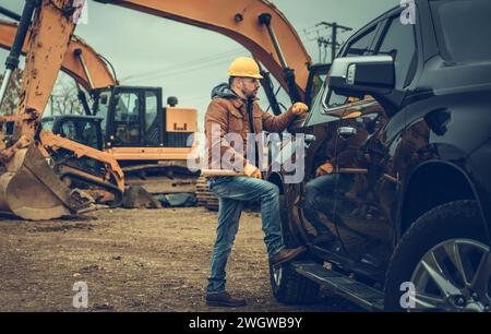 Supervisore del cantiere caucasico dei 40 anni che soggiorna accanto al suo pick-up. Escavatori in background Foto Stock