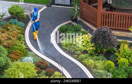 Proprietario di casa caucasico a 40 anni che pulisce i suoi percorsi di mattoni da giardino nel cortile con idropulitrice Foto Stock