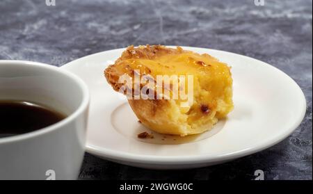 Un pastel de nata non mangiato o un dessert all'uovo portoghese su un piatto bianco. Pastel de Belm è una piccola torta con una crosta croccante di pasta sfoglia e una crema pasticcera Foto Stock