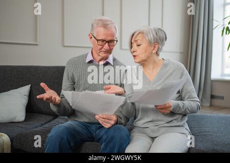 Triste stanco, deluso, coppia di anziani di mezza età siedono con un documento cartaceo. Infelice anziano maturo donna che legge banconote che gestiscono le finanze bancarie calcolano le tasse pianificazione prestito pagamento pensione Foto Stock