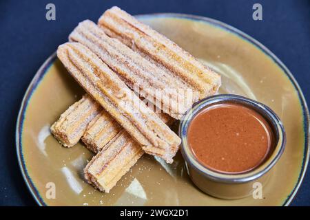 Churros freschi con salsa al cioccolato su piatto rustico Foto Stock