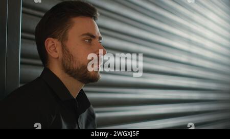 Vista laterale un uomo caucasico serio, un imprenditore di affari, un venditore, un dirigente d'affari, un uomo d'affari penoso, un uomo sulla parete nera Foto Stock