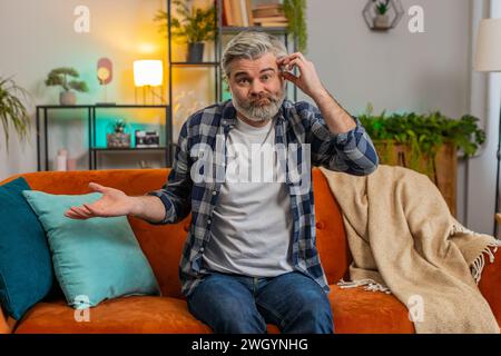 Non so cosa dire. Confuso uomo anziano di mezza età che si sente imbarazzato per la domanda ambigua che dubita che non abbia idea di essere incerta a casa. Un ragazzo maturo si siede sul divano nel soggiorno. Foto Stock