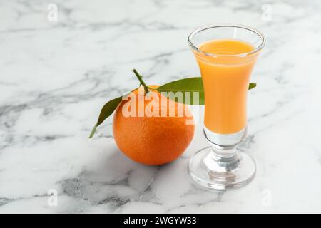 Delizioso liquore al mandarino in bicchierino e frutta fresca su un tavolo in marmo bianco, primo piano. Spazio per il testo Foto Stock