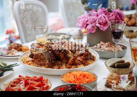 Delizioso pilaf uzbeko tradizionale con tenero agnello e verdure fresche, servito con vivaci insalate e sottaceti. Presentato splendidamente e appetitoso Foto Stock
