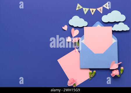 Busta con cartoline vuote e fiori di garofano su sfondo blu. Celebrazione della giornata internazionale della donna Foto Stock